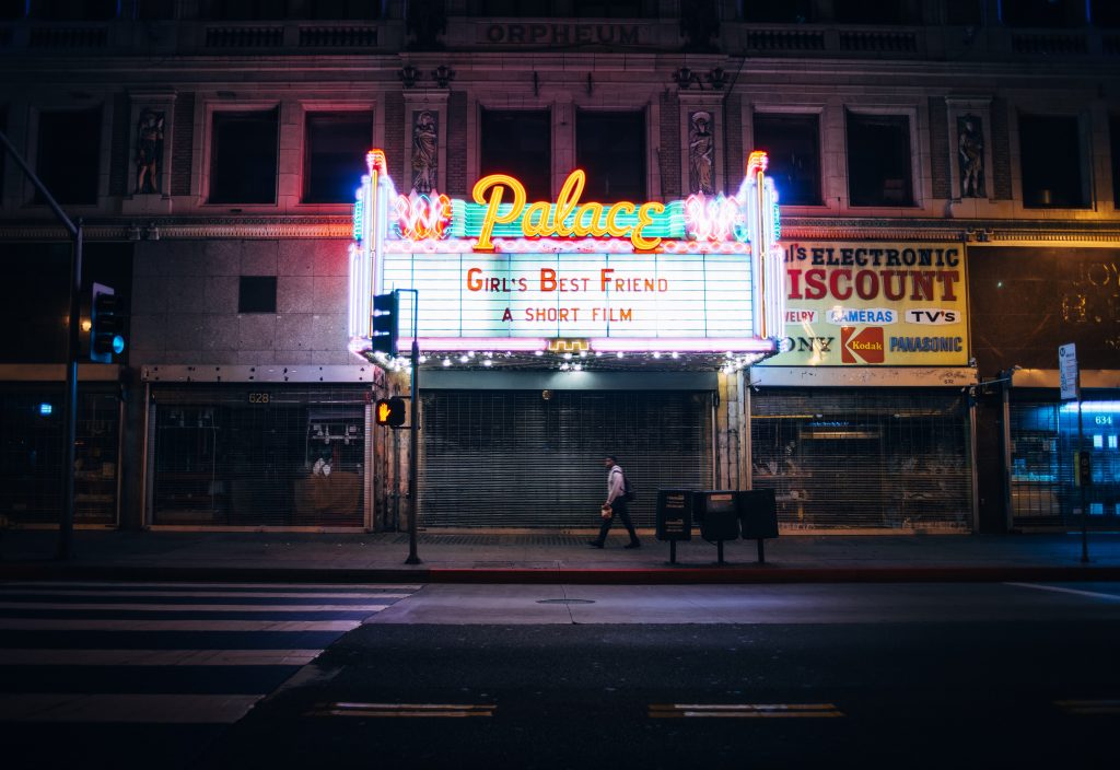 Brightly lit theater sign on a quiet street promoting the screening of a short film. Hosting a screening at an existing theater may give you temporary use of their employees as event help rather than using volunteers.