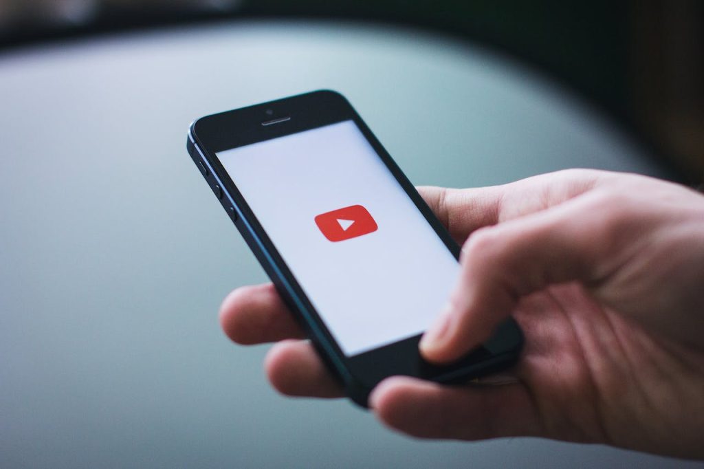  hand holding a phone opening the youtube app for virtual fundraising guide