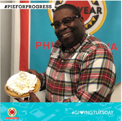 Pie for Progress picture featuring a man holding a pie in front of a City Year Philadelphia logo.