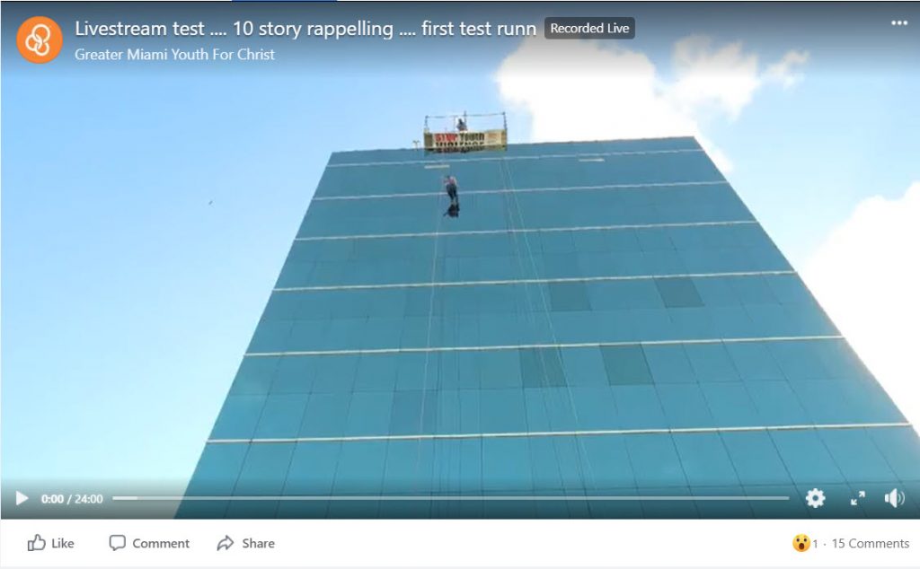 A still image from the livestream recording of Greater Miami Youth for Christ's Over the Edge fundraising event. It shows a rappeller starting descent down a skyscraper.