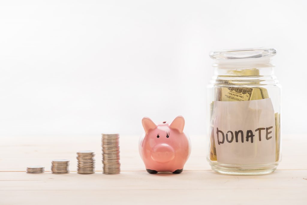 stacks of quarters, a piggy bank, and a glass jar that says "donate" with cash inside