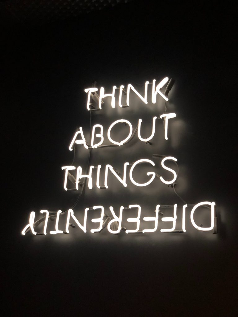 Neon sign that says think about things differently. Differently is upside down.