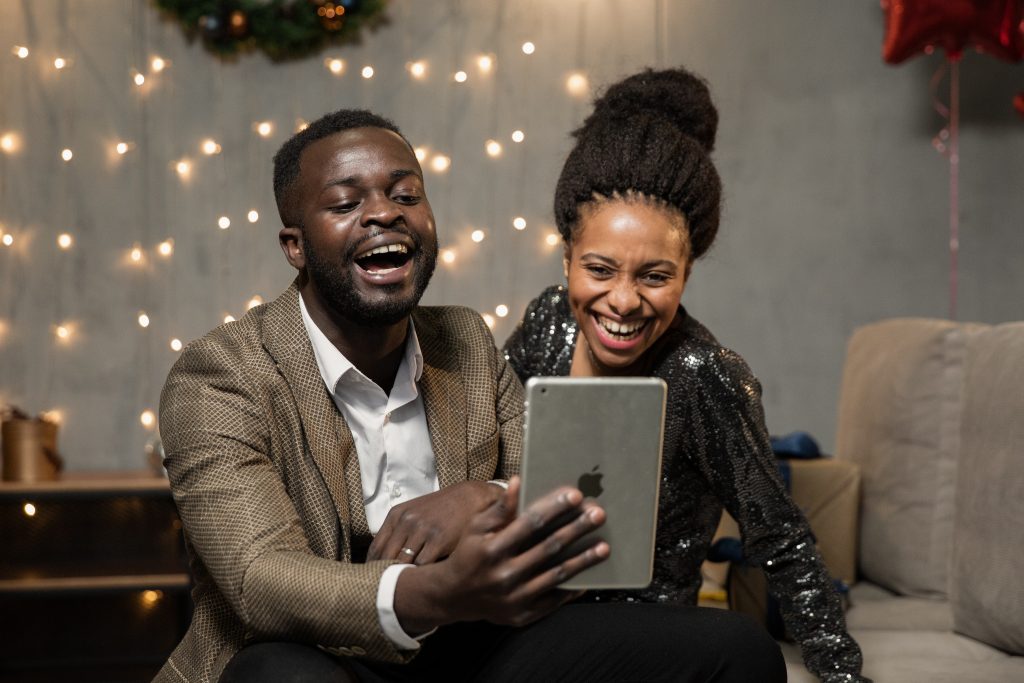 Two people laughing as they enjoy taking part in a virtual party from their cell phone.