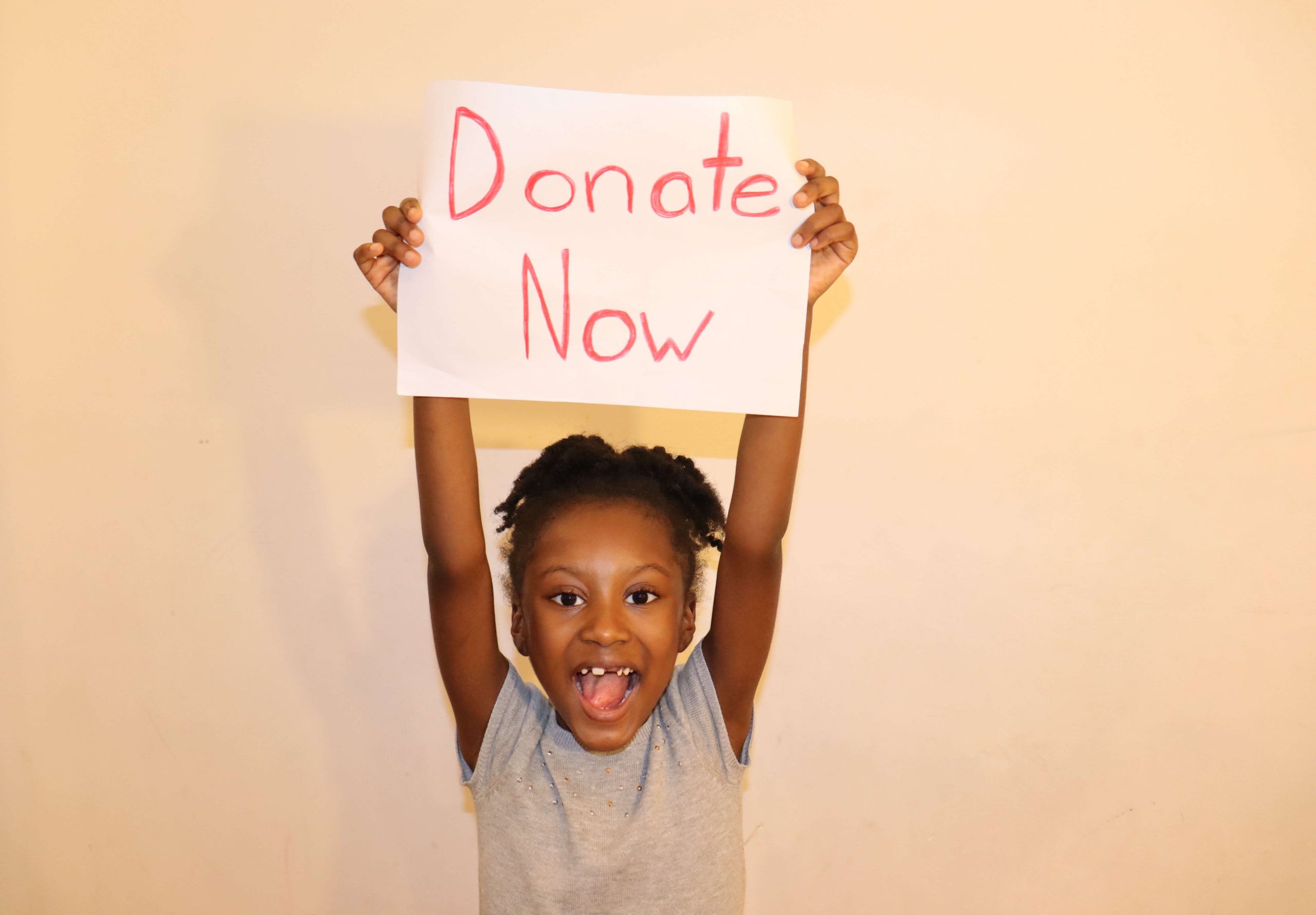 girl holding a sign that reads "donate now."