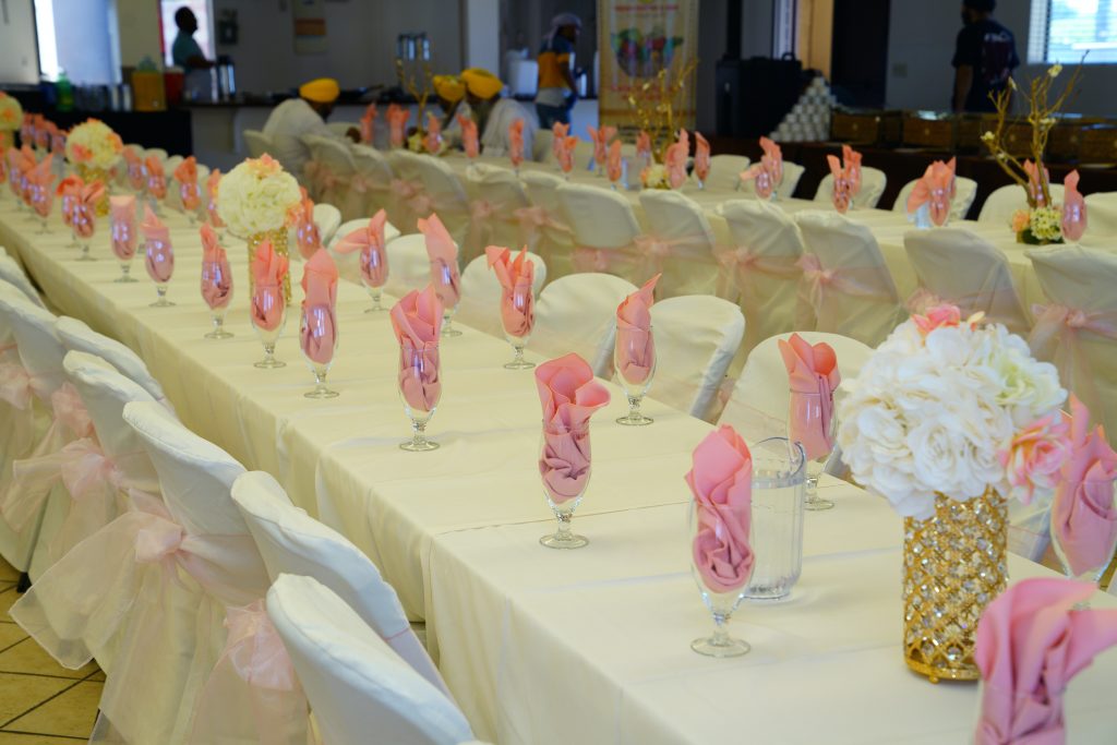 Fundraising gala seating featuring a pink and white theme with flowers as centerpieces and bows on the chairs.