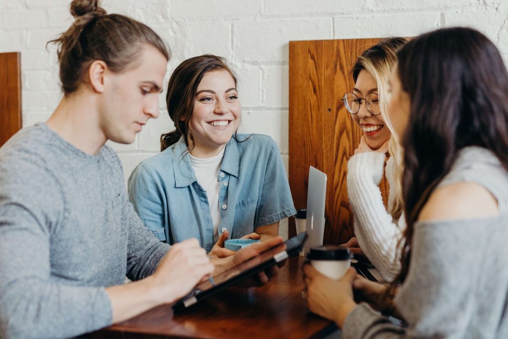 Four young people with iPads and laptops, smiling at each other.