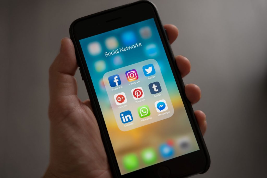 closeup of a hand holding a smartphone open to social media app icons