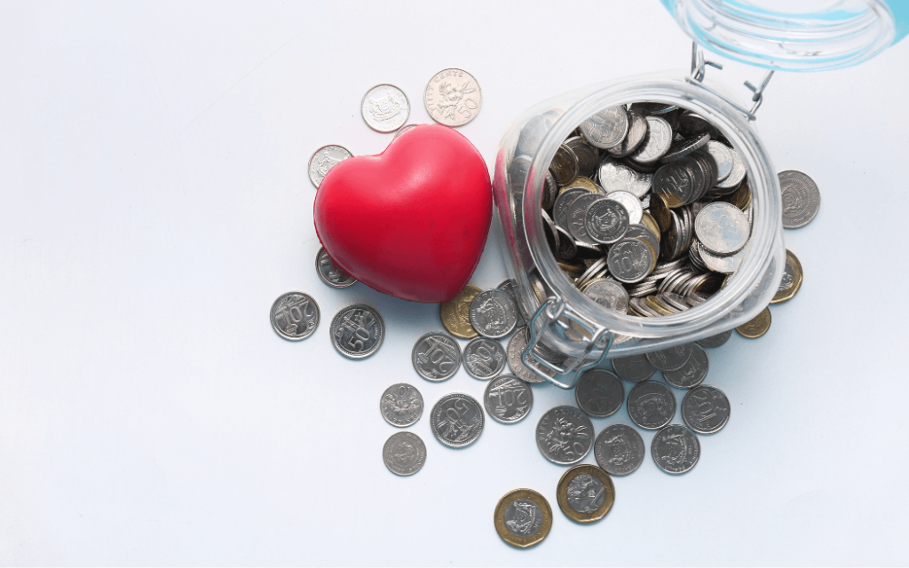 Donation jar with coins inside and outside of the jar and a heart toy next to the jar