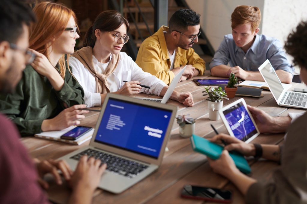 Group of coworkers sitting around a table working on software training on computers and tablets