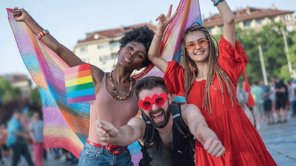 three people holding rainbow pride flags and celebrating pride month