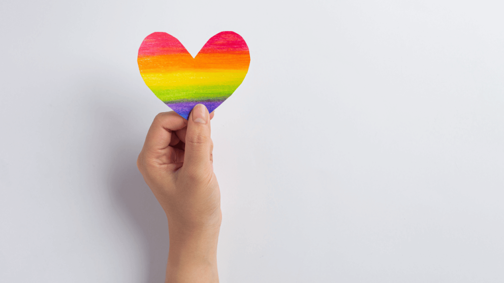 close up of a hand holding a rainbow-colored heart in celebration of pride month