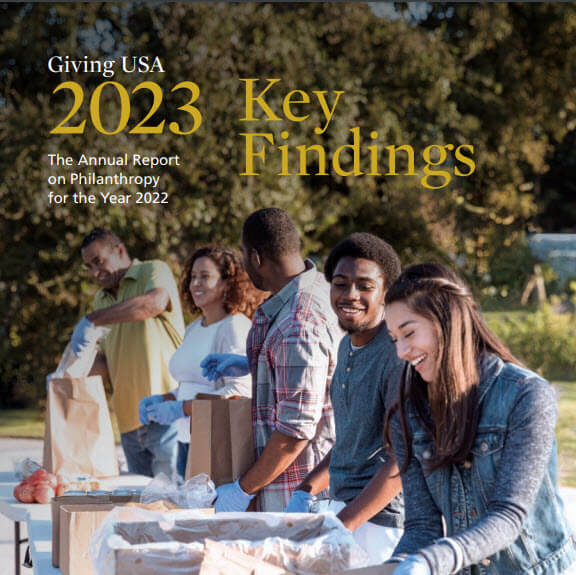Giving USA 2023 Report cover image featuring volunteers passing out food at a park.