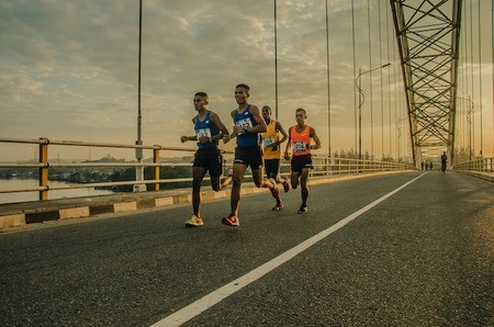 Four people running across a bridge during a virtual runathon