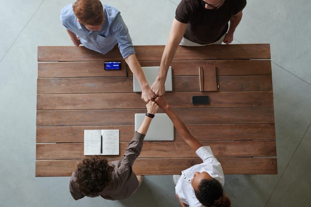 Four people fist bumping over a table in celebration of their nonprofit collaboration