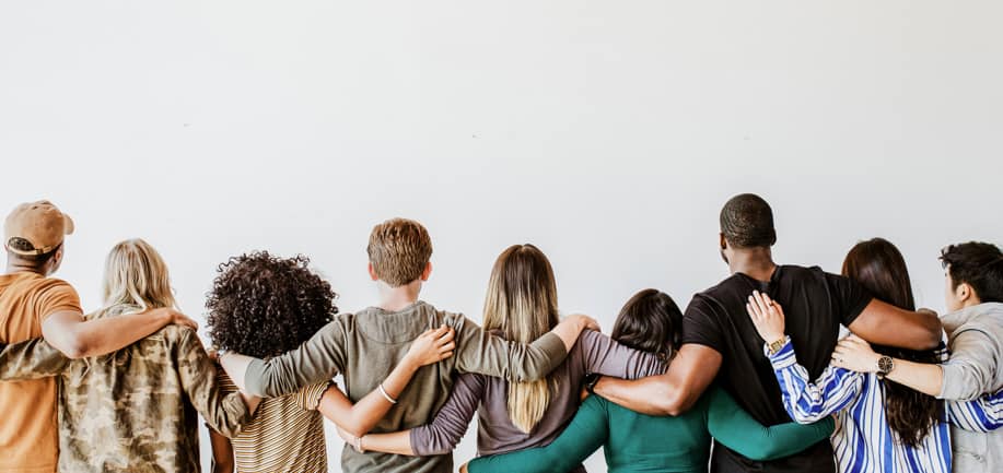 rear view of people standing next to one another with arms around each other, indicating inclusion