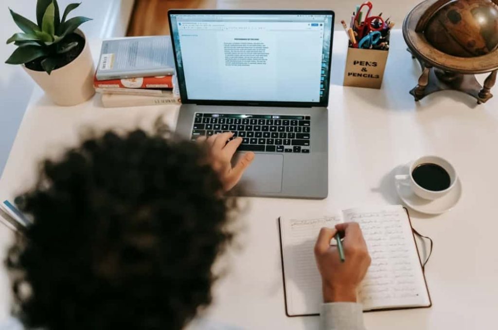 woman writing a nonprofit sponsorship letter on a computer and in a notebook at a desk